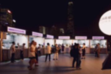 Blurred image of a street market with many people at night. The background has a blur effect and the city lights create bokeh.