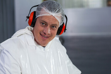 Male technician standing in production hall in protective coverall hairnet and earmuffs, copy space