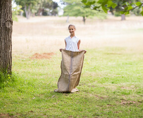 Female child standing in grassy meadow holding tall burlap sack with stitched stripes
