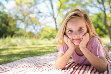 Girl lying on striped picnic blanket in park, propping chin on hands, copy space