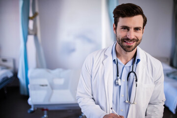 Doctor holding pen and writing on clipboard in bright hospital ward near bed and curtain