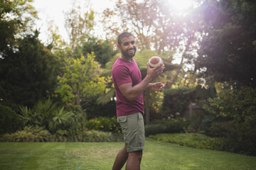 African American man smiling and holding football on backyard lawn under bright sunlight