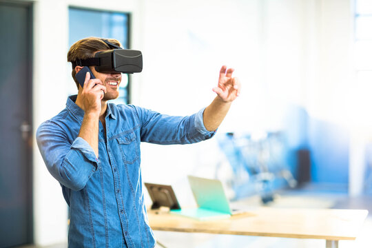 Man wearing VR headset holding smartphone interacting at office desk with laptop, copy space