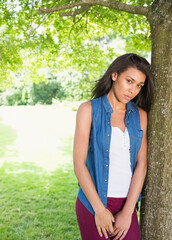 African American woman leaning on tree trunk in park wearing denim shirt and shades, copy space