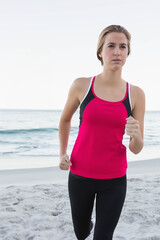 Female runner running on sandy beach wearing pink athletic top, black leggings and white shoes