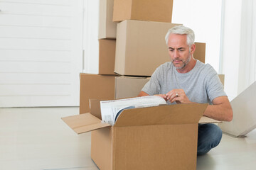 Man kneeling on floor in bright home unwrapping bubble-wrapped item from cardboard box, copy space