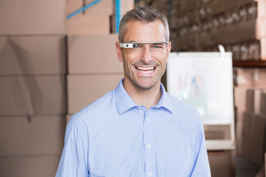 Mid adult man wearing AR glasses and blue shirt, standing in warehouse by stacked boxes, whiteboard