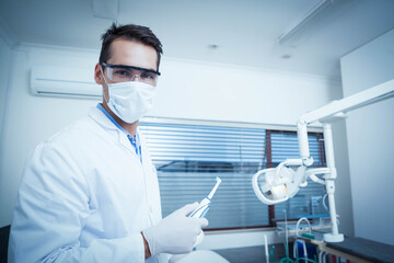 Male dentist wearing lab coat with mask, gloves holding polishing tool in clinic, copy space