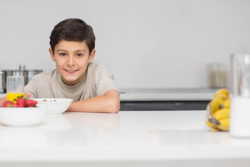 Boy around ten smiling and leaning on white counter in kitchen by cereal and orange juice