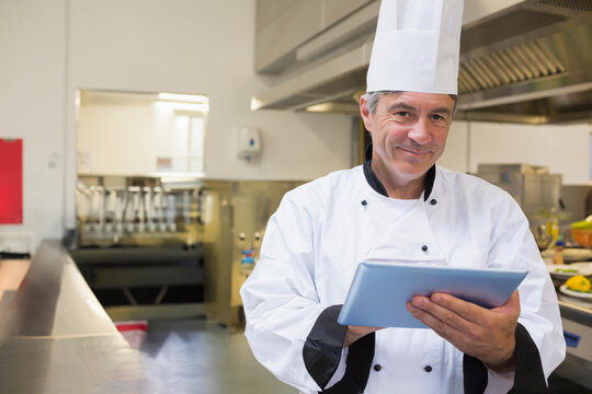Holding tablet male chef in professional kitchen with steel counter, ventilation hood, copy space