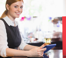 Standing at bar, server in her twenties wearing uniform holding tablet and wine glass, copy space