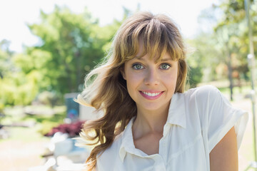 Smiling adult woman wearing white button-up blouse standing outdoors in green park