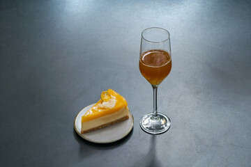 a pice of orange cake pie and orange juice mocktail in flute glass on black table in garden