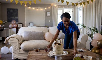 African American woman leaning over coffee table at home arranging dishes around 30th birthday cake