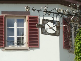 Weathered wooden restaurant sign displaying utensils near red shutters, window framing historic...