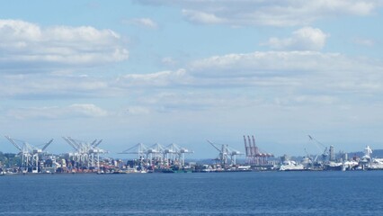 Cargo cranes and ships populate the industrial Seattle waterfront, under a blue sky dotted with...