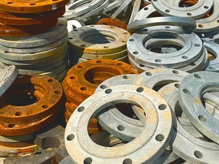 A large pile of industrial pipe flanges, both new and rusted, in an outdoor storage area. This...