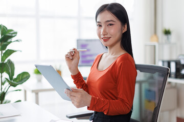 Asian Female business person using digital tablet and laptop or remote working at office, looking...