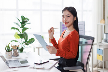 Asian Female business person using digital tablet and laptop or remote working at office, looking at digital tablet learning training, studying online thinking Financial and Accounting concept.
