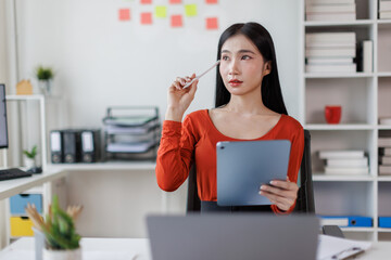 Asian Female business person using digital tablet and laptop or remote working at office, looking...