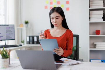 Asian Female business person using digital tablet and laptop or remote working at office, looking...
