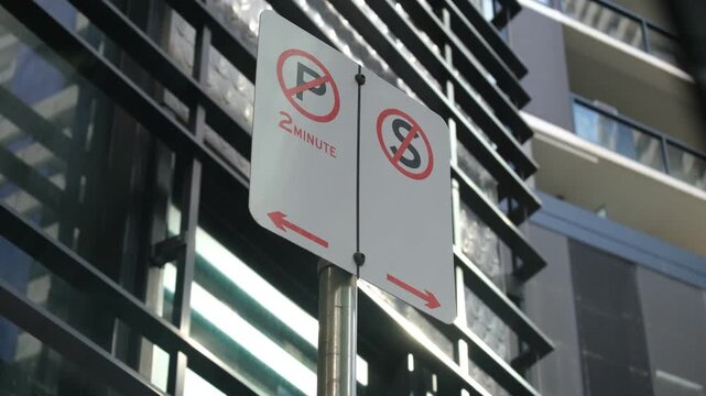 A parking restriction sign in Melbourne, Australia, with a 2-minute no-parking zone and a no-stopping zone with directional arrows against modern apartment buildings in CBD.