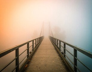 Obraz premium Suspension bridge with wooden planks stretches into dense fog, creating mysterious and adventurous atmosphere, surrounded by misty forest and steel cables