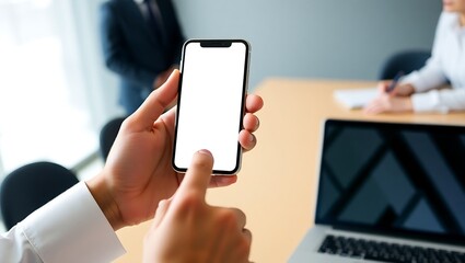Businessman's hands holding a modern smartphone with a blank white screen for mockup. Professional using a mobile device in an office meeting.