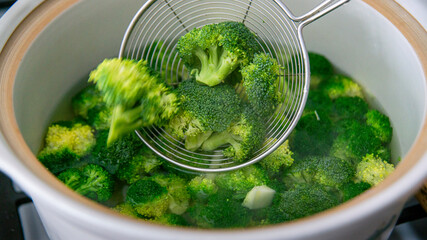 Fresh Broccoli Florets Boiling in Water &ndash; Healthy Cooking Preparation at home and collecting Broccoli by a Asian Strainer Ladle Stainless Steel Wire Skimmer Spoon.