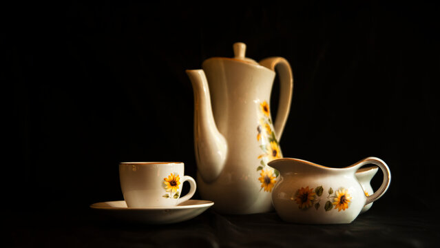 Vintage, old teapot with a teacup and sugar cup, isolated against the background with light falling from the right side &mdash; artistic and representing old heritage.