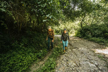 Fototapeta premium Mother and daughter dressed in hiking clothes, walking along a trail in the middle of the rainforest.