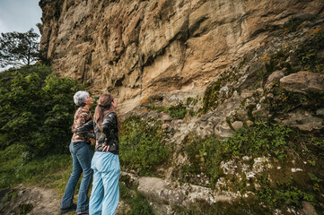 Mother and daughter dressed in hiking clothes, walking along a cliff to find cave paintings.