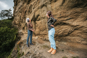 Mother and daughter dressed in hiking clothes, walking along a cliff observing cave paintings.