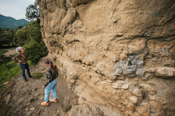 Mother and daughter dressed in hiking clothes, walking along a cliff observing cave paintings.