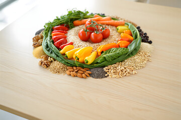 Vibrant healthy food arrangement: colorful vegetables, grains, nuts, and seeds on a light wood...