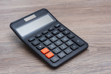 Modern black digital calculator with LCD display on a natural wooden desk surface. Professional...