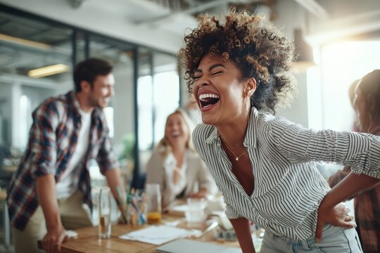 Joyful group of young professionals laughing together in a modern office setting, showcasing teamwork, collaboration, and a positive work environment with vibrant and energetic interactions