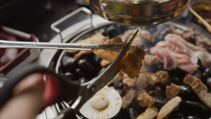 Hand cooking smoked grilled pork on iron grill pan in Korean BBQ in restaurant. Traditional Korea style food barbecue pork belly steak on charcoal grill.