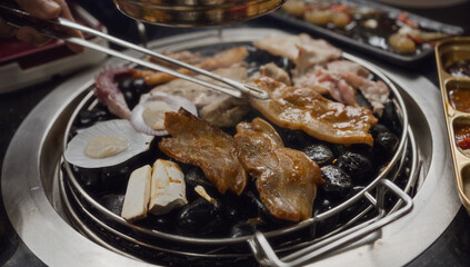 Hand cooking smoked grilled pork on iron grill pan in Korean BBQ in restaurant. Traditional Korea style food barbecue pork belly steak on charcoal grill.