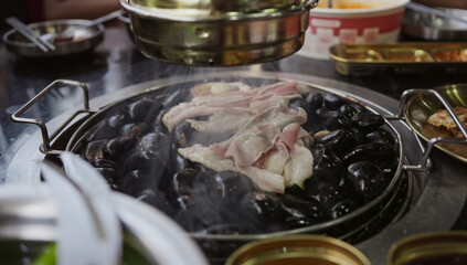 Hand cooking smoked grilled pork on iron grill pan in Korean BBQ in restaurant. Traditional Korea style food barbecue pork belly steak on charcoal grill.