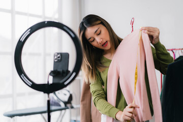 Asian female vlogger measuring clothes while streaming live, promoting online fashion business