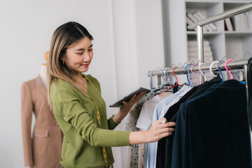 Obraz premium Asian fashion designer using digital tablet checking clothes on clothing rack