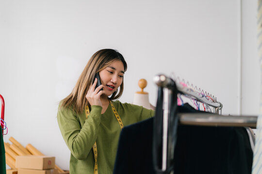 Fashion designer talking on phone and choosing clothes on rack