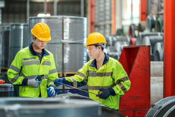 Two male factory workers wea yellow safety helmets and reflective jackets inspecting industrial...