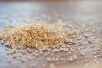 Sugar granules scattered on wooden surface close up