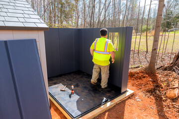 Construction worker in bright vest in forested area under assembling storage shed