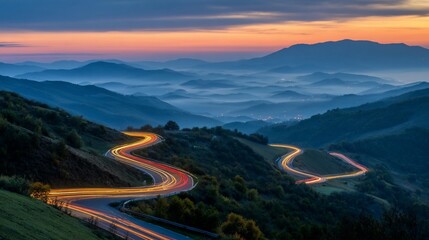 Winding mountain road at dawn. Light trails curve through valleys. Mist over hills. Sunrise colors the sky