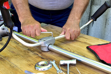 A man repairs a brush cutter. He tightens the bolts holding the brush cutter handles with a wrench.