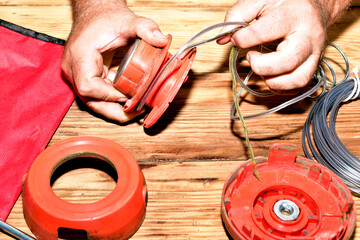 Repairing a petrol trimmer. A man winds the cutting line onto the spool.
