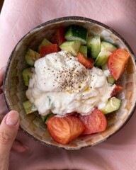 Healthy vegetable salad with cucumber, tomato, and yogurt dressing in a handmade ceramic bowl